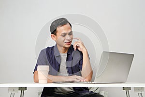 joyfull happy asian man at workplace while sitting in front of laptop computer. on isolated background