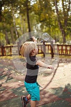 Joyfull little boy burst soapbubble in a jump with a hand