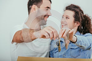 Joyfull wife and husband standing behind the big carton box, , holding together in front of the camera keys to their new