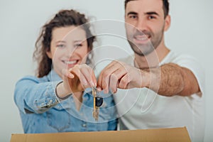 Joyfull wife and husband standing behind the big carton box, , holding together in front of the camera keys to their new