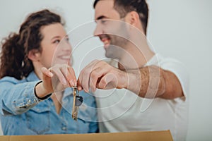 Joyfull wife and husband standing behind the big carton box, , holding together in front of the camera keys to their new