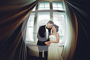 Joyfyl newlyweds stand between the curtains