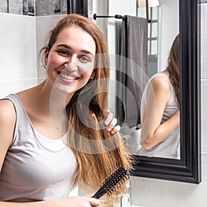 Joyous beautiful young woman standing, brushing her long dry hair