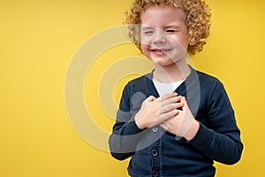 Joyous boy holding hands on chest with closed eyes and grateful gesture on face