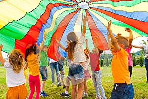 Joyous classmates jumping under colorful parachute in the summer outdoors photo