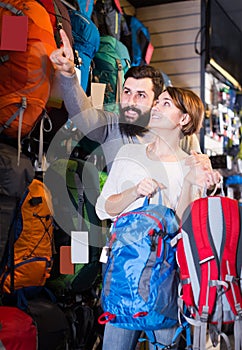 joyous couple examining rucksacks in sports equipment store