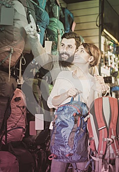 Joyous couple examining rucksacks in sports equipment store