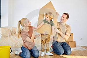 Joyous family and kid boy playing in new home with cardboard boxes on floor. Portrait