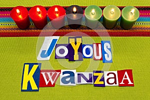 JOYOUS KWANZAA text word collage typography, seven candles and multi colored fabric on green woven fabric, African American holida
