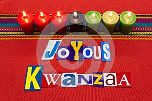 JOYOUS KWANZAA text word collage typography, with seven candles and multi colored fabric on red woven fabric, African American hol