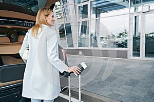 Joyous lady with boarding ticket near open car trunk