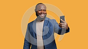 Joyous man using smartphone to take selfies, studio background