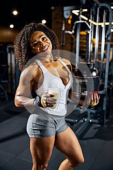 Joyous sportswoman with a protein shake posing for the camera