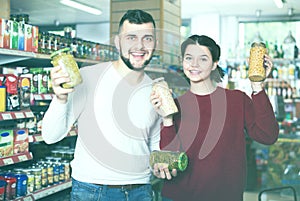 Joyous young family choosing purchasing canned food for week at