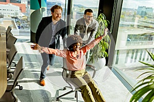 Jubilant Office Celebration Captures Colleagues Spontaneous Chair Race in Sunlit Room
