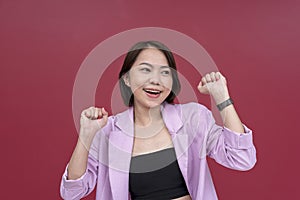 A jubilant short-haired young asian woman celebrating success. Giddy with joy. Studio shot with burgundy background photo