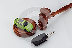 Judge gavel and green toy car with keys on a white table close-up. Symbol of law, justice and car auction