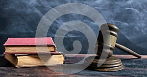 Judge gavel, old books and reading glasses on a wooden table, black board background. 3d illustration