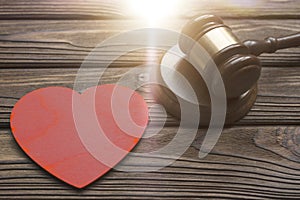 A judge hammer, a wooden heart shape on a wooden background.