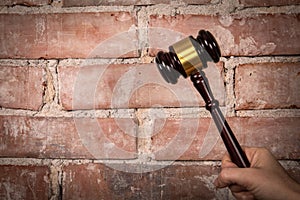 Judge hand holding gavel. Red brick background