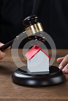 Judge Holding Gavel On House At Desk