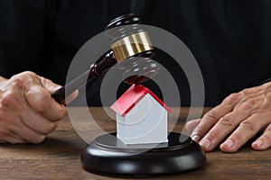 Judge Holding Gavel On House At Desk