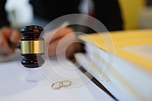 Judge holding wooden gavel near two wedding rings close-up