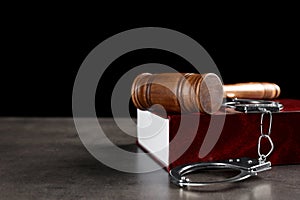 Judge`s gavel, handcuffs and book on grey table against black background. Criminal law concept