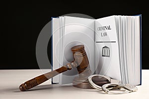 Judge`s gavel, handcuffs and Criminal law book on table against black background