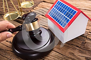 Judge`s Hand Hitting Mallet By Solar Model Home On Table