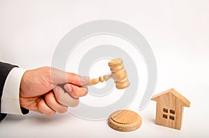 The judge`s hand is holding a hammer next to the wooden house. trial of real estate. Elimination and alienation of bankruptcy, co