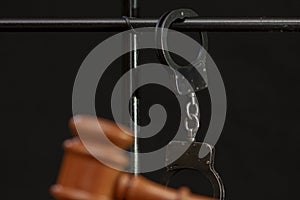 The judge`s wooden hammer for sentencing against the background of bars and handcuffs. Concept: court session, trial, sentencing.