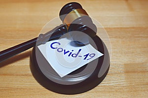 Judges gavel or law mallet and word covid-19 on sound block on wooden background.