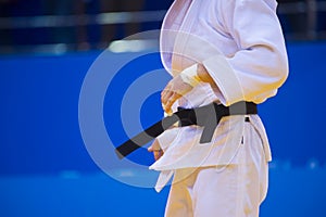 Judo fighter poses in white kimono with black belt. Japanese judo and jiu jitsu