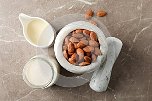 Jug of almond milk, mortar with almond seeds on brown background, top view