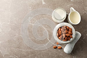 Jug of almond milk, mortar with almond seeds on brown background, top view