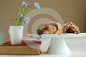 Jug with flowers forget-me-not on vintage book and croissants