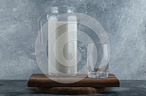 Jug of fresh milk and glass of water on wooden board