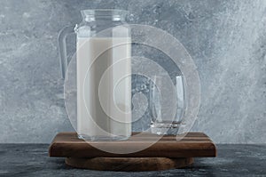 Jug of fresh milk and glass of water on wooden board