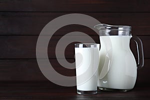 Jug and glass with fresh milk on wooden table. Space for text