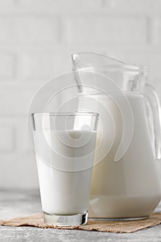 jug and glass of milk on table with white brick wall as background