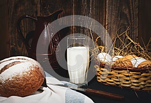 Jug and glass of milk on a wooden table basket with eggs and buckwheat bread