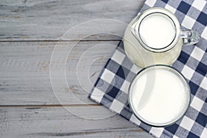 Jug and glass of milk on a wooden table, top view