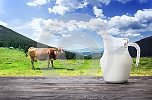 Jug of milk against background of cow and mountain pasture