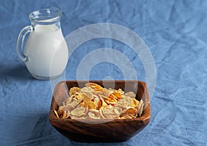 Jug with milk , corn cereals in a wooden plate on blue tablecloths Close up. Shallow depth of field