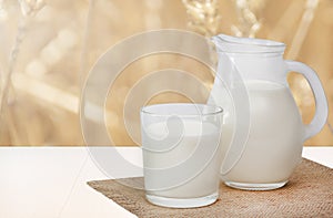 Jug of milk and glass milk on napkin on white wooden table