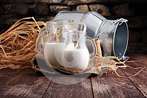 A jug of milk and glass of milk on a wooden table.