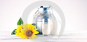 A jug of milk and glass of milk on a wooden table and flower