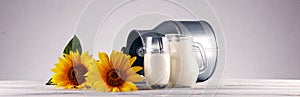 A jug of milk and glass of milk on a wooden table and flower