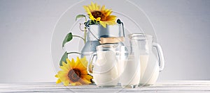 A jug of milk and glass of milk on a wooden table and flower